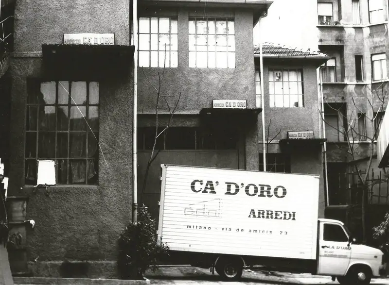 Un camion bianco col nome dipinto, «Ca’ d’Oro arredi, Milano, via De Amicis», parcheggiato davanti a un magazzino