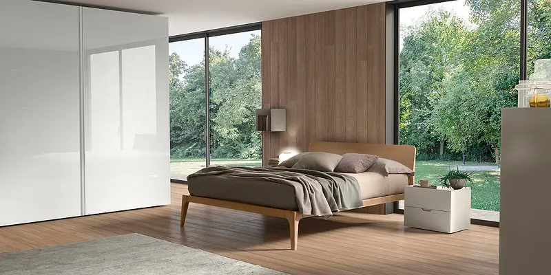 Una camera da letto con un letto in legno chiaro davanti a una grande vetrata sul verde